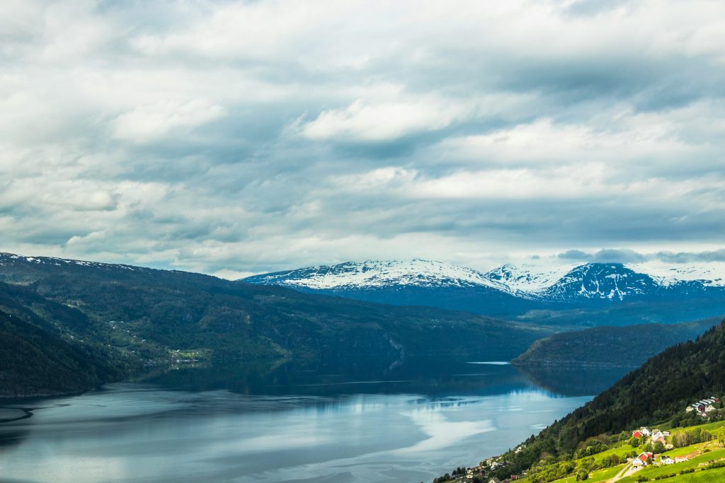 Breathtaking landscape of snow-capped Norwegian mountains and a tranquil lake reflecting the cloudy sky.